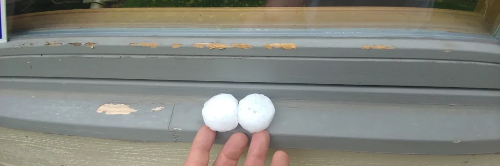 Large hailstones and visible window paint damage illustrating when to report hail damage on roof by Elite Roofing & Solar