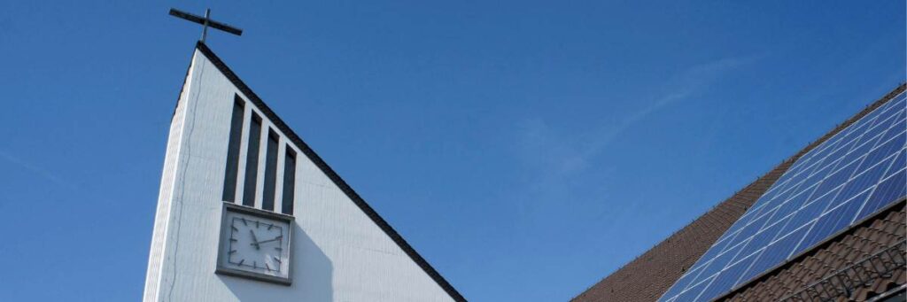 A church steeple with a clock and cross stands against a blue sky, adjacent to a roof equipped with solar panels, suggesting the potential for an Xcel Solar Battery Storage Program, installed by Elite Roofing & Solar.