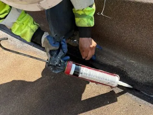 Technician applying high-grade sealant to commercial roof seam for effective repairs by elite-solar in Colorado