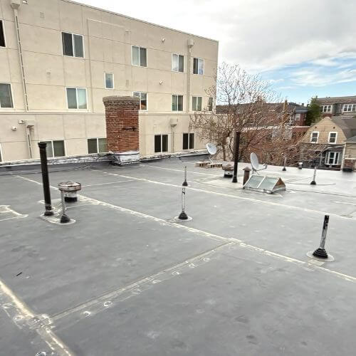 Flat rubber membrane roof on a multifamily building with vents and skylights, showing how minimal roof pitch affects roof replacement cost in Denver. Example of roofing work by Elite Roofing & Solar.