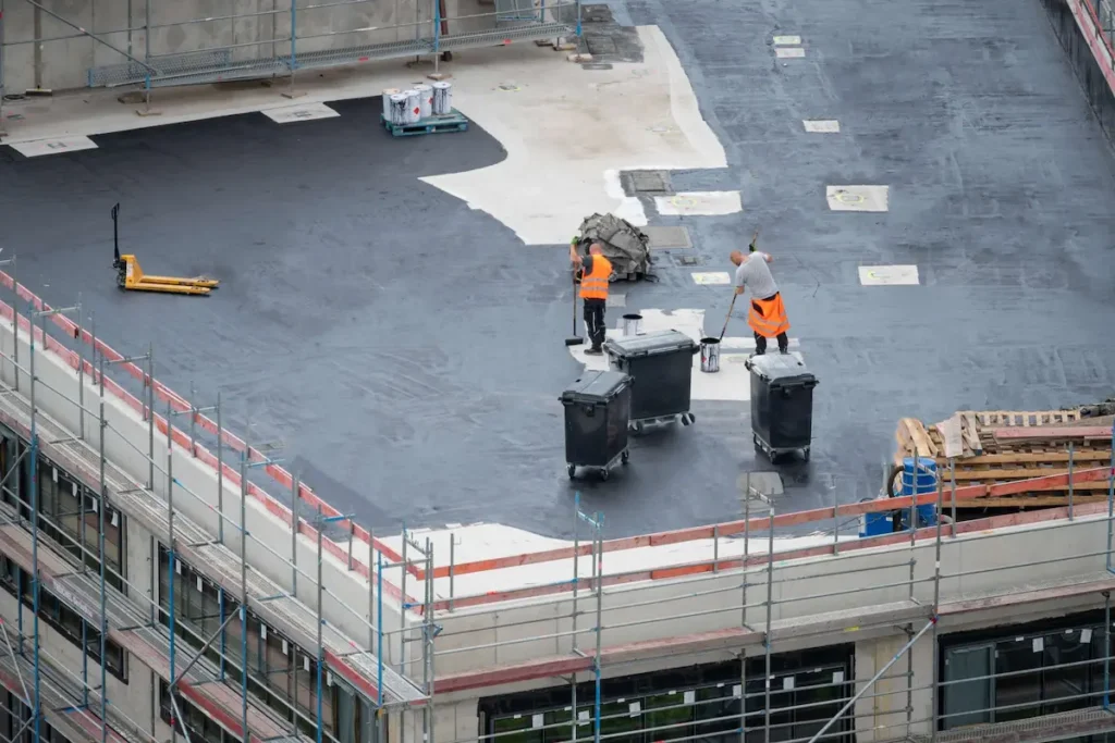 Commercial roofing specialists applying professional roof coatings with rollers on a large flat roof for maximum protection and durability by elite-solar