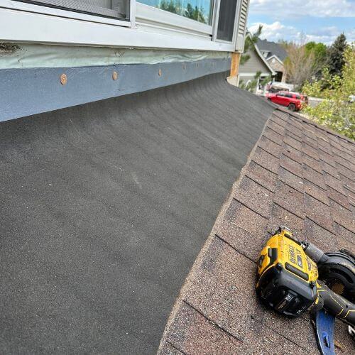 Close-up view of a sloped roof with new shingles, flashing installation, and repair tools, highlighting how roof pitch can impact roof replacement cost. Image taken during a residential roofing project in Denver by Elite Roofing & Solar.