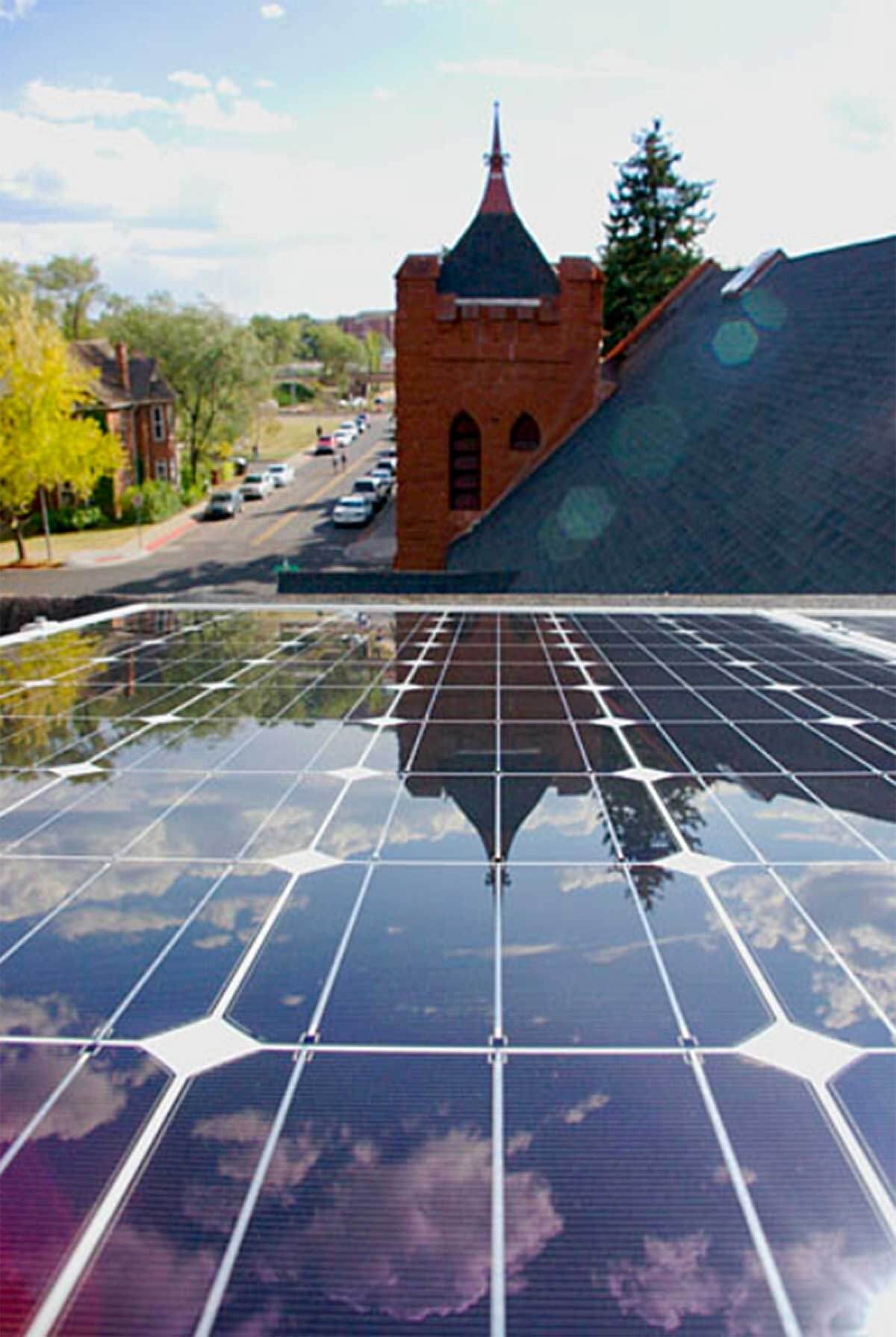 A close-up of solar panels on a rooftop, reflecting the sky and a nearby brick church steeple, illustrating a sustainable energy solution that could be part of the Xcel Solar Battery Storage Program.