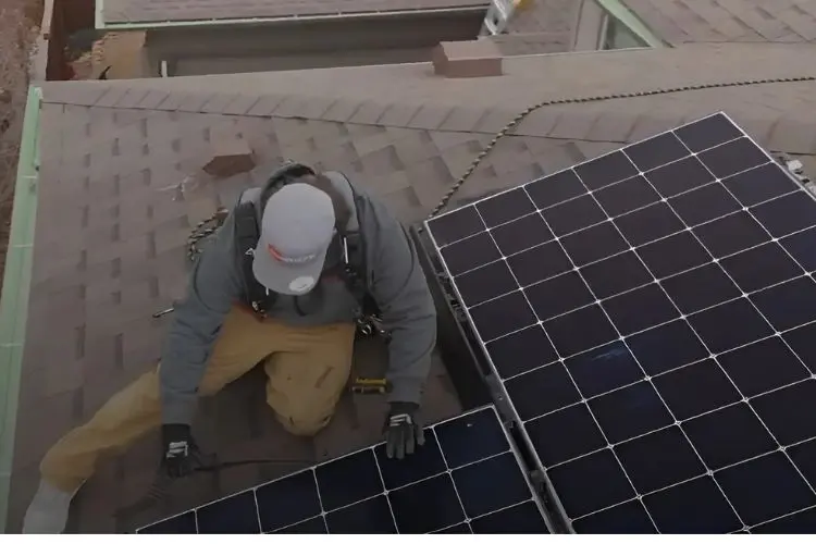 Technician installing solar panels on residential asphalt shingle roof, using safety harness by elite-solar in Colorado