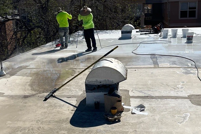 Team members applying commercial roof coating on flat rooftop by Elite Roofing and Solar in Gaco