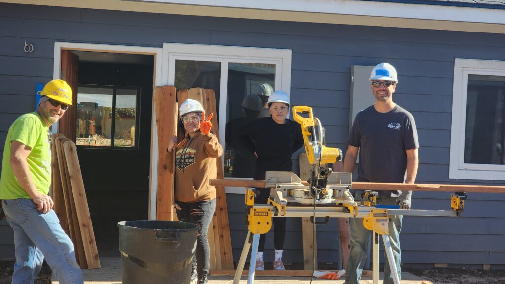 Elite Roofing & Solar team members behind a circular saw installing a new fence for a Habitat for Humanity House in Denver, CO.