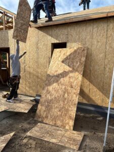 Elite Roofing & Solar team member lifting roof decking to place on top of a home under construction for charity in Denver, CO