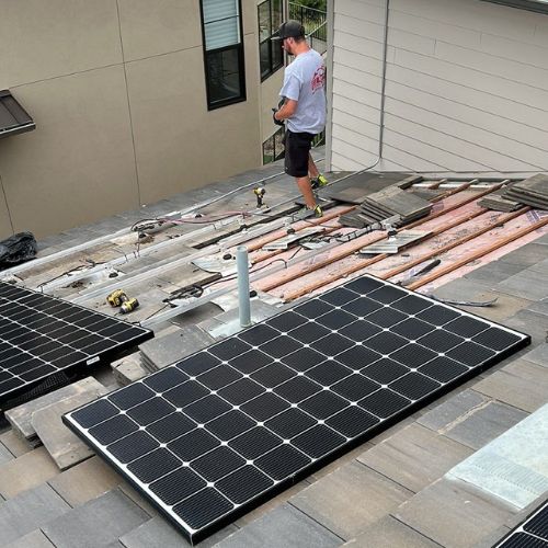 Rooftop solar installation in progress with one panel mounted and additional rails visible, while an Elite employee stands nearby overseeing the work in Denver