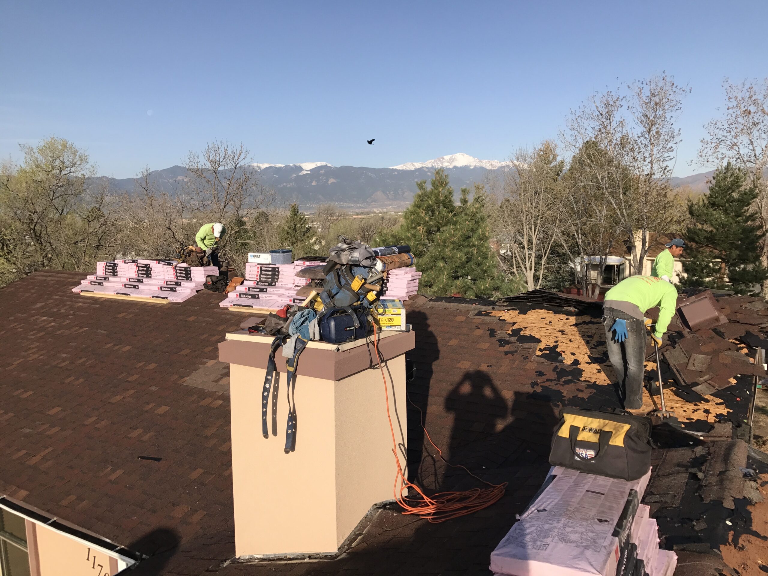 A roofing crew removes old shingles and organizes new material bundles to determine accurate roof square measurements. Roof square measurements in Denver by Elite Roofing and Solar