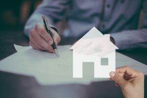 a person signing insurance paperwork with an image of a home overlaid